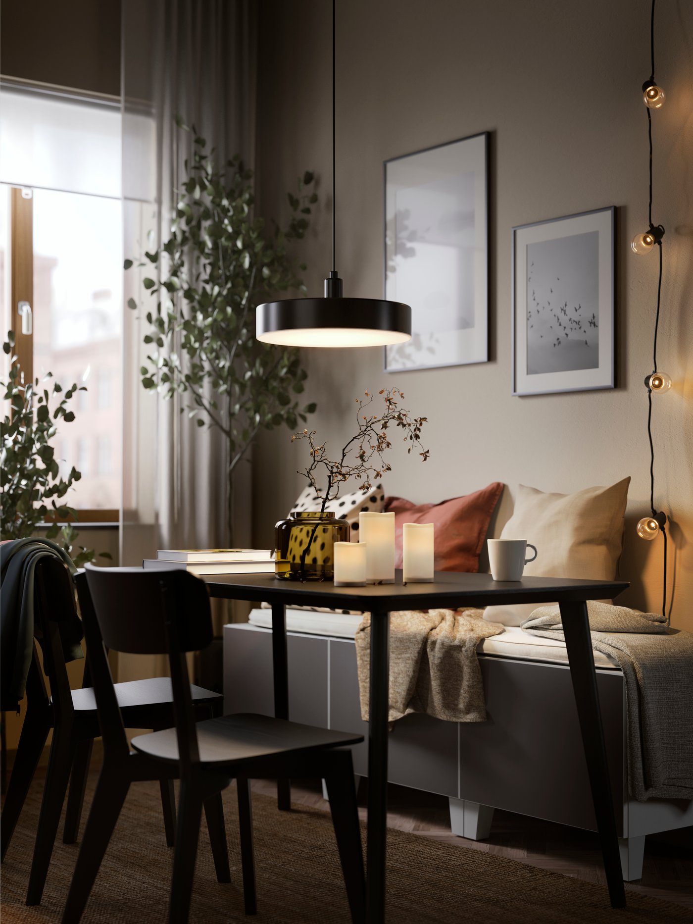 A NYMÅNE LED pendant lamp hangs over a black LISABO table and two black LISABO chairs which stand on a LOHALS rug.