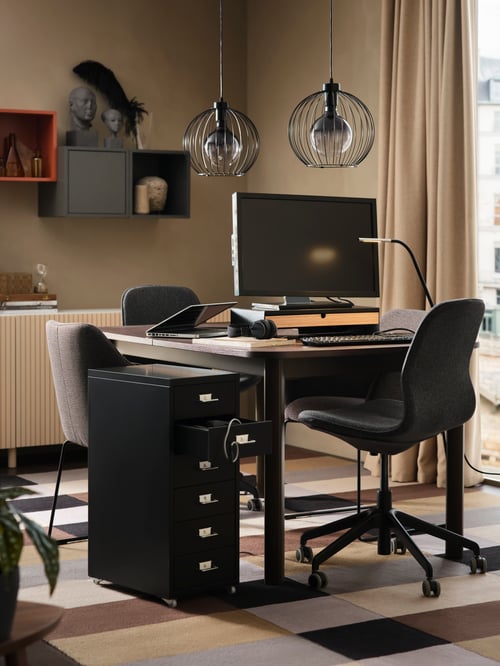 Ein STRANDTORP Ausziehtisch als Arbeitsplatz, u. a. mit einem Monitor auf einem Ständer und einer Leuchte. Davor steht ein Drehstuhl.