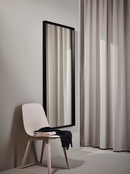 Entrée avec des murs gris clair, un miroir avec un cadre noir, des rideaux assombrissants, une chaise et des vêtements.