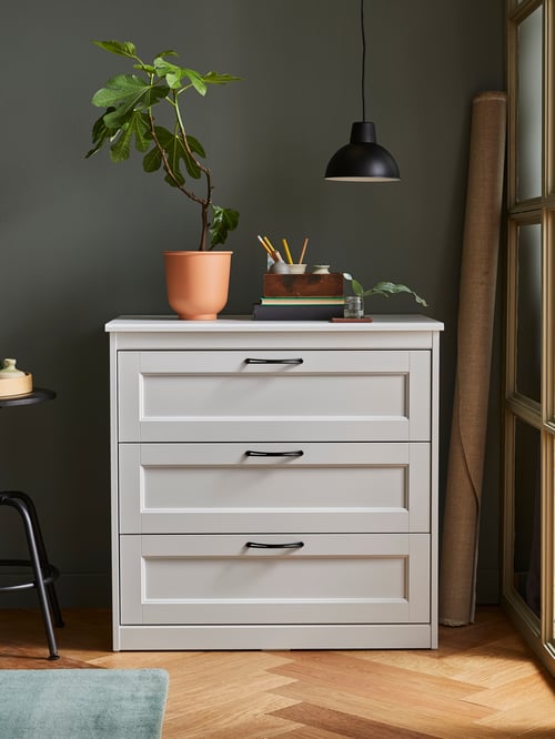 A white SONGESAND chest of drawers with a red-brown plant pot on top, underneath a black pendant lamp.