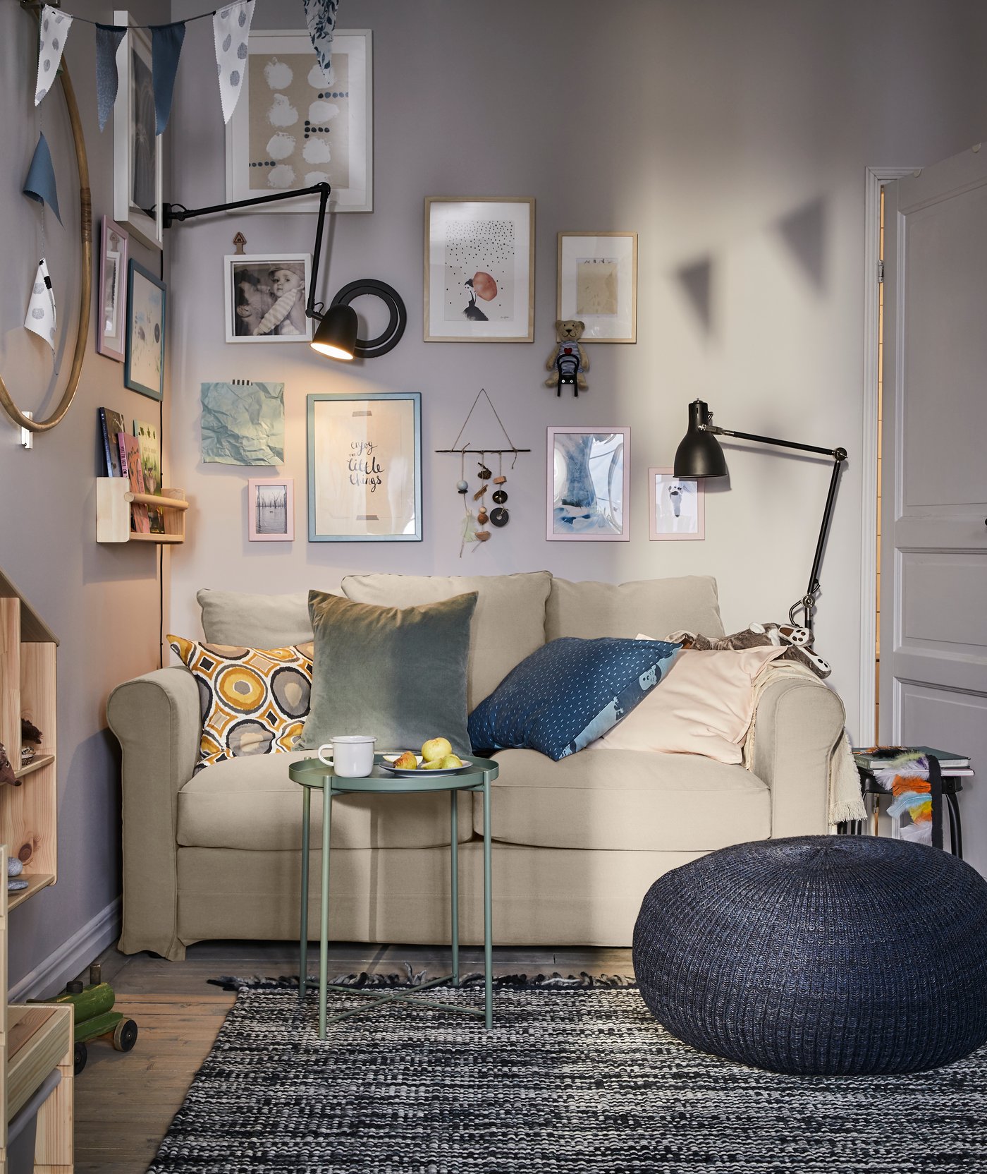 Ein Wohnzimmerbereich mit GRÖNLID 2er-Sofa Inseros weiss, dunkelblauem Sitzkissen und einem grünen Tablettisch. Beiderseits sind schwarze Leuchten zu sehen.