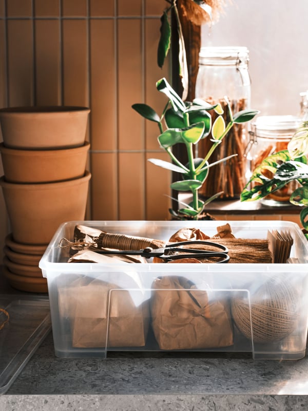 Three MUSKOTBLOMMA plant pots are stacked on top of each other on top of four saucers next to a transparent SAMLA box.