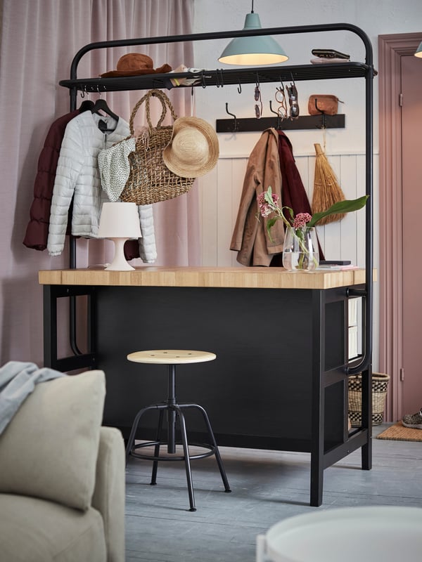 A VADHOLMA kitchen island with rack in black/oak used as a room divider in a hallway and to store clothes and accessories.
