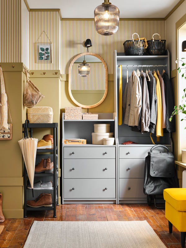 A yellow hallway with a grey HAUGA open wardrobe and chest of drawers in it. Coats are on the rail and a mirror is beside it.