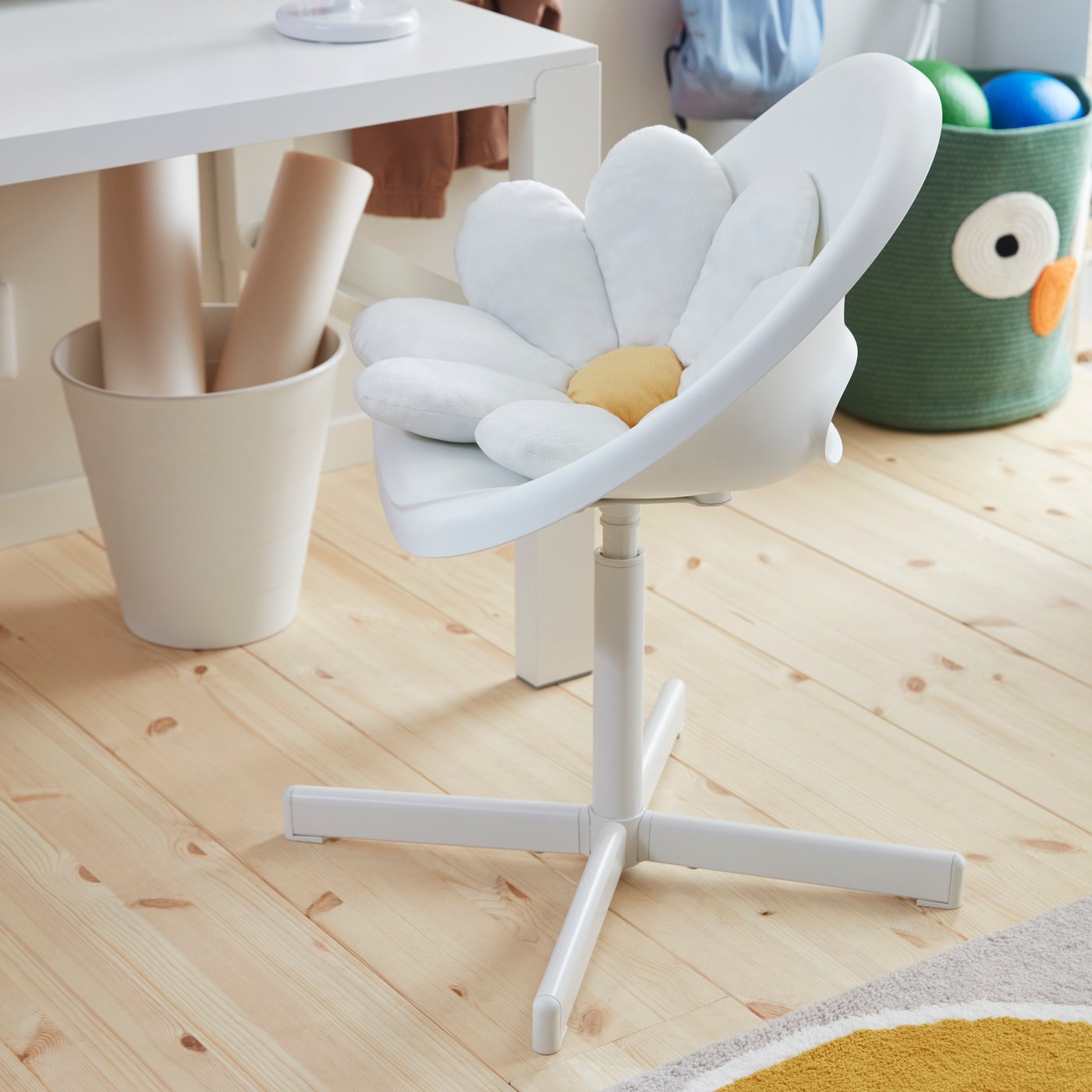 A white LOBERGET/SIBBEN children’s desk chair holding a daisy cushion, placed next to a PÅHL desk in a children’s room.