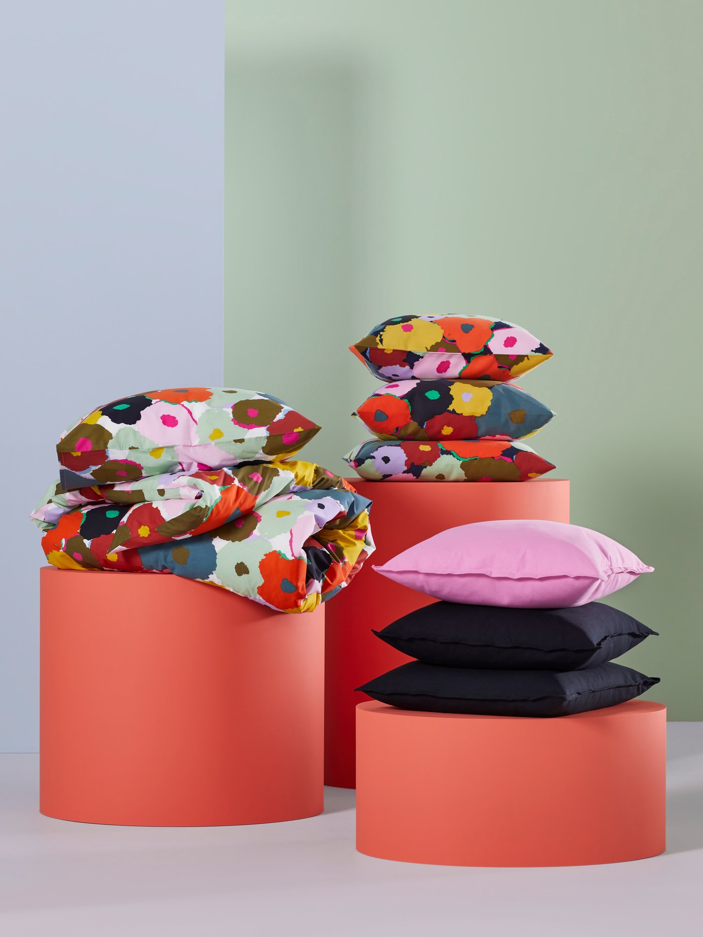 Tres podios rojos. Uno tiene una funda nórdica/de almohada MURREVA. Otro tiene cojines MURREVA y el tercero cuenta con cojines GURLI en negro/rosa.