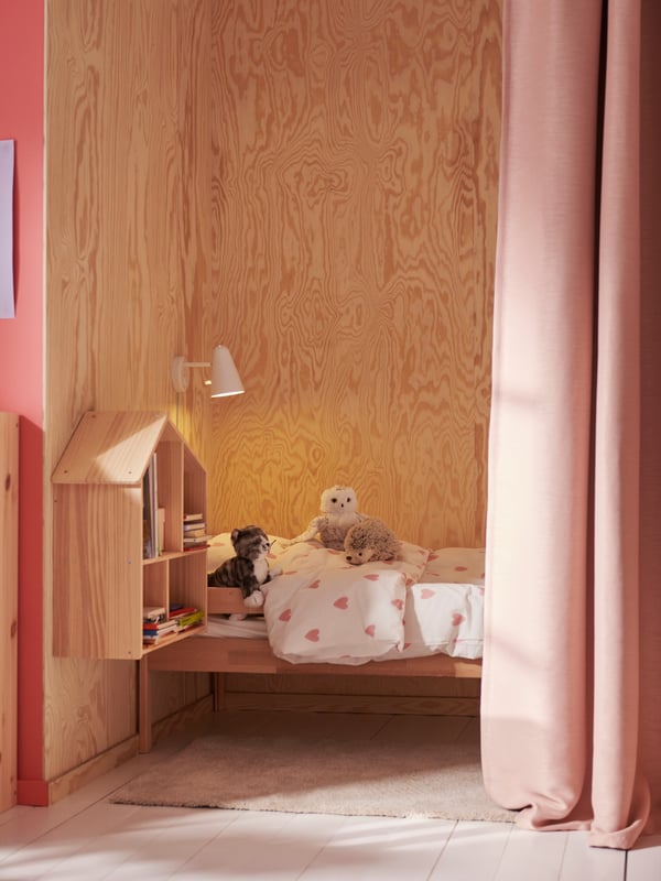 Ein SNIGLAR Juniorbettgestell mit Stützbrett steht in einer Nische mit einem Vorhang. Darüber befindet sich eine FUBBLA LED-Wandleuchte. Auf dem Bett liegt Bettzeug in BARNDRÖM Bettwäsche.
