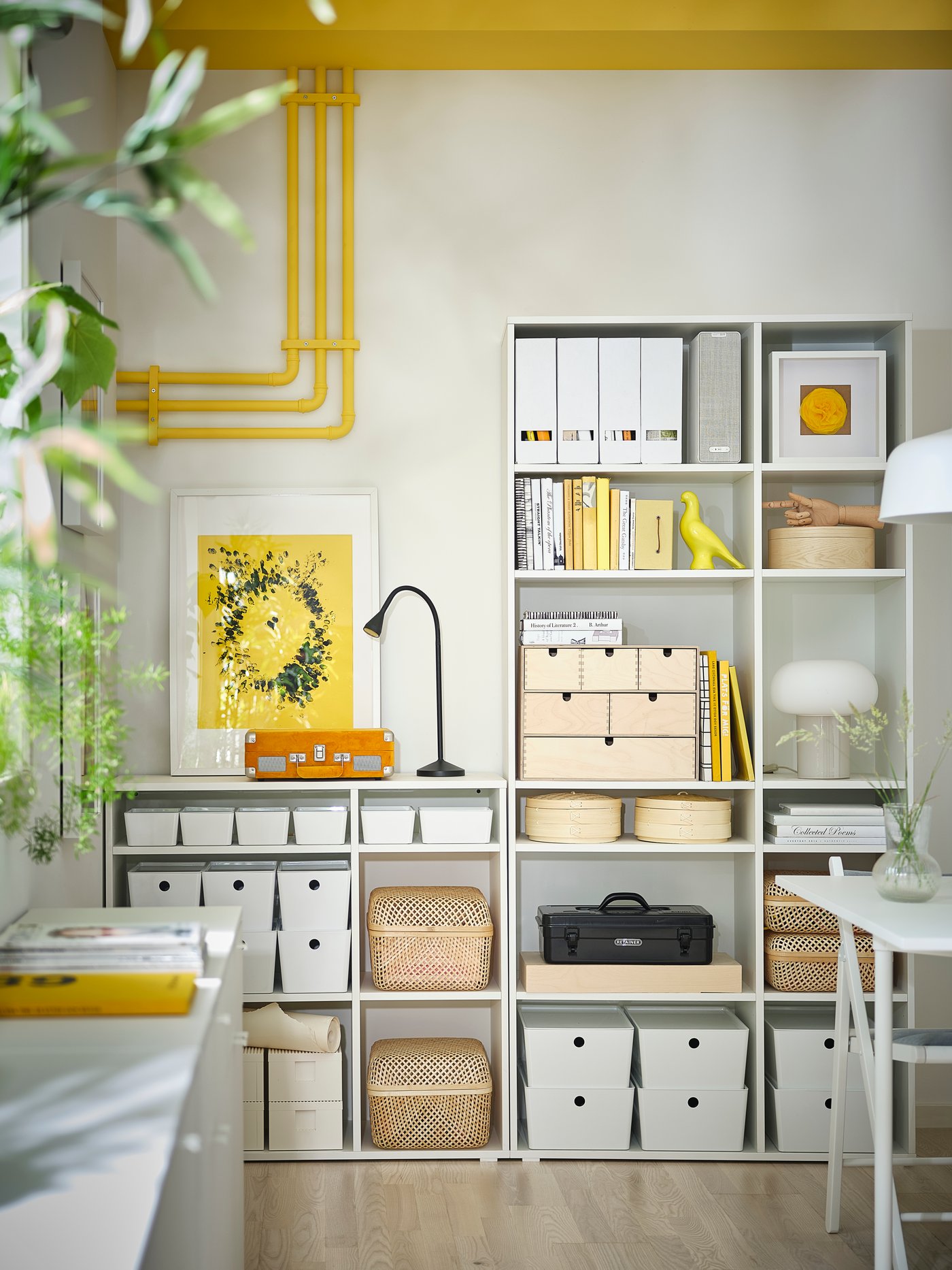 Pared de una cocina con una estantería alta de madera blanca con diez estantes, cajas blancas con tapa y cajas de bambú.
