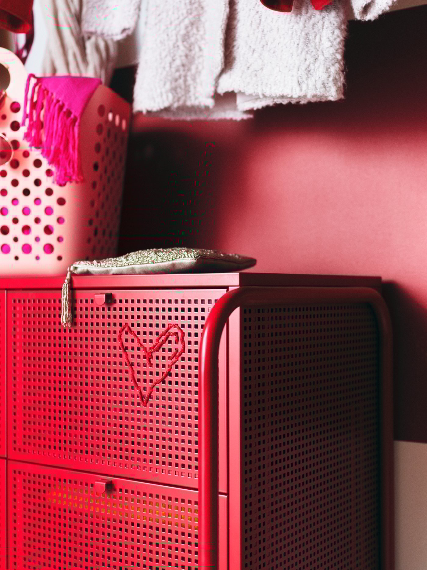 A red NIKKEBY chest of drawers with a red heart embroidered on it and a pink SLIBB flexible laundry basket on top.