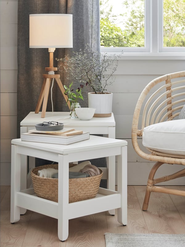 Une lampe de table LAUTERS avec une base en frêne massif sur une table basse HAVSTA blanche à côté d’une fenêtre et d’un fauteuil BUSKBO.