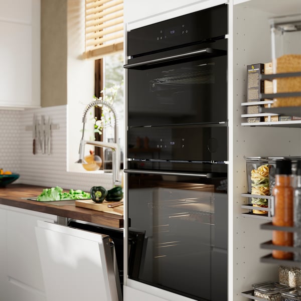 Forno ventilado SPJUTBO e forno ventilado com função de micro-ondas colocados numa cozinha com frentes VOXTORP em branco mate.