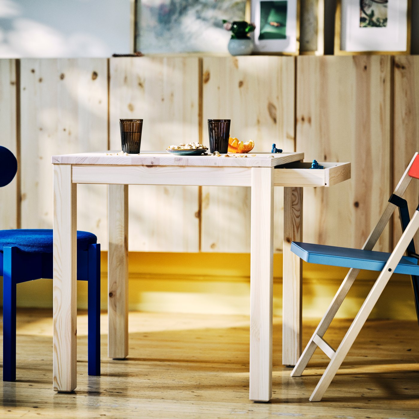 Light wood table with glasses, snack plate and chairs on a sunlit wooden floor.