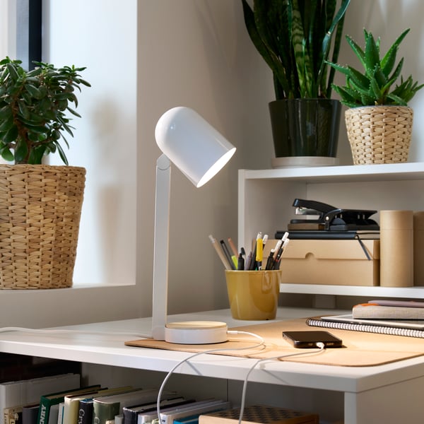 A corner of a room with a white BILLY desk filled with desk accessories and lit up by a white ENSMÄRKE desk lamp.