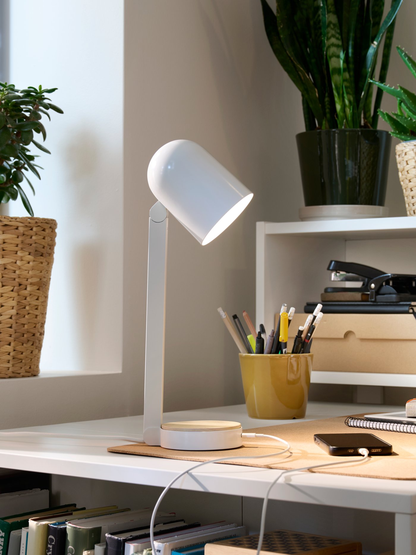 Gela baten izkinan dagoen BILLY idazmahai zuri bat, idazmahairako osagarriz betea eta ENSMÄRKE idazmahaiko lanpara zuri batek argitua.