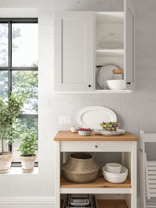 Weiße Küche mit TORNVIKEN Kücheninsel aus Holz, METOD Hängeschrank mit zwei Türen, FLÅDIS Korb, VARDAGEN Teller, EGENDOM Schüsseln und Geschirr.