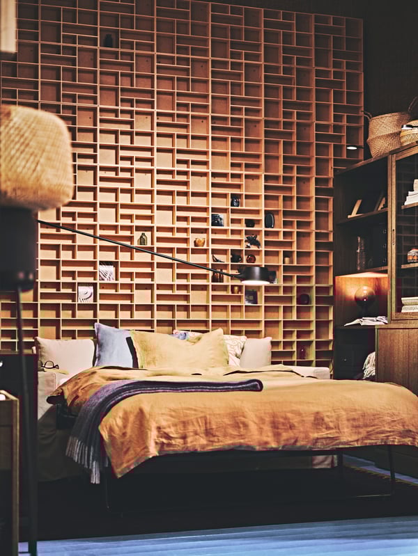 An off-white HYLTARP two-seat sofa bed made up of a bed against a lattice-shaped shelf featured wall.