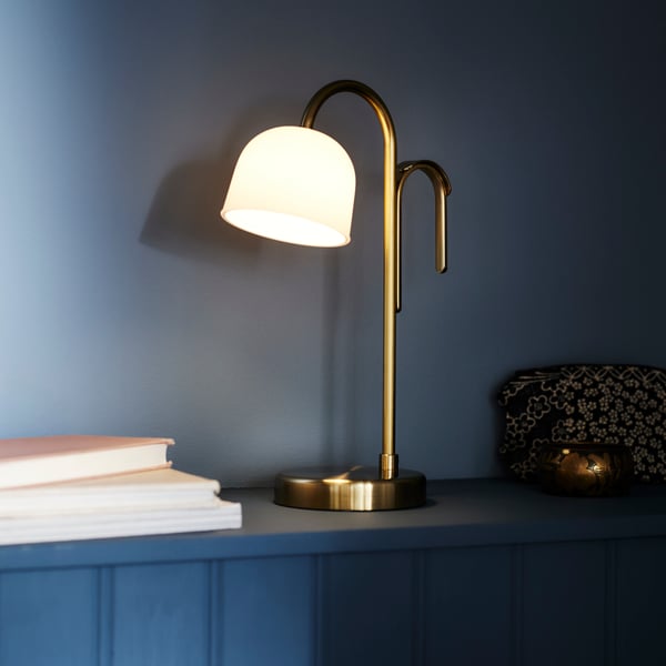 A battery-operated brass/opal white glass TVÅMASTAD LED portable lamp in the bedroom
