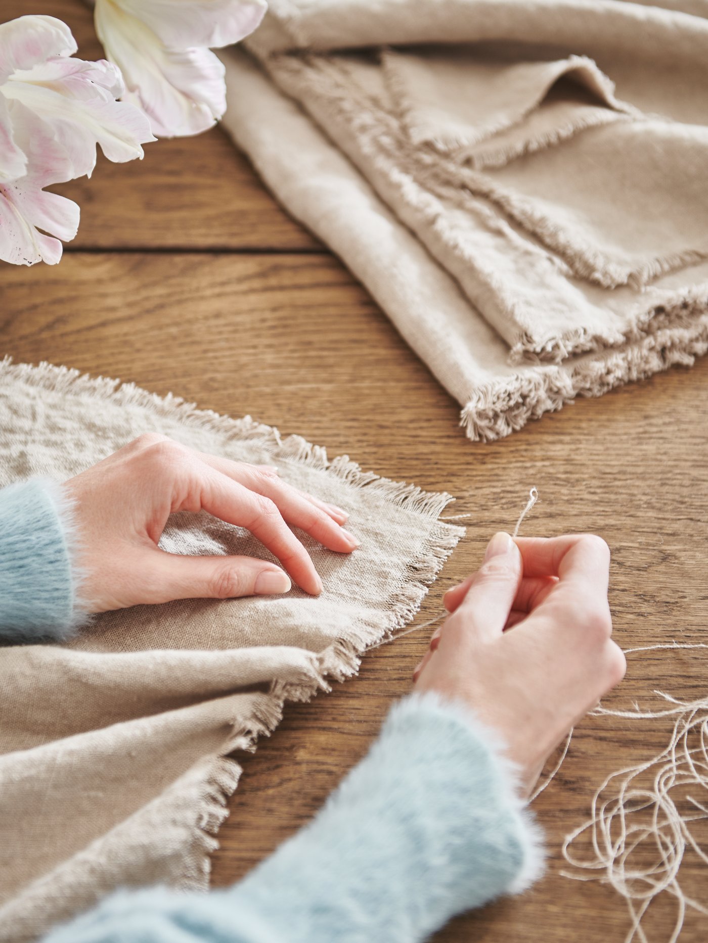 Mani di una persona che sfrangiano i bordi di un runner realizzato con il tessuto AINA color naturale.