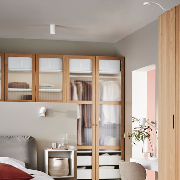 A bedroom with a NYMÅNE ceiling spotlight, a NYMÅNE wall/reading lamp, a NYMÅNE work lamp and YTBERG cabinet lighting.