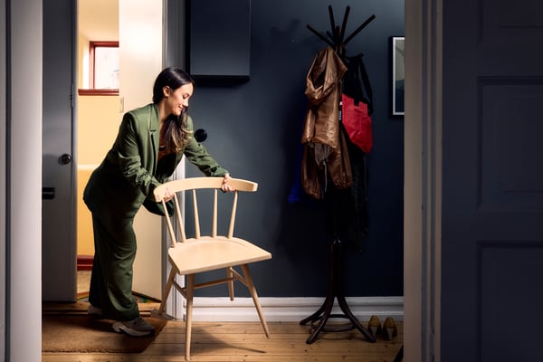 Persona movent una cadira de fusta clara a l'entrada de casa, preparant el moble per canviar-lo de lloc o treure'l a l'exterior.
Escena interior acogedora con perchero y prendas colgadas junto a la puerta.
