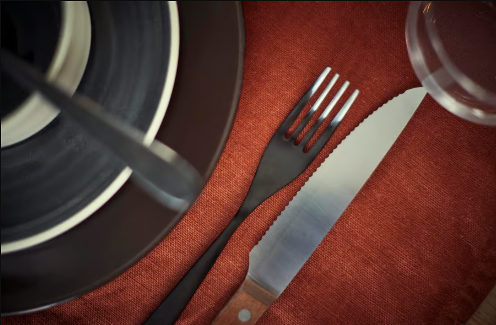Nahaufnahme von Messer, Gabel, Glas und schwarzem Geschirr auf rotem Platzset.