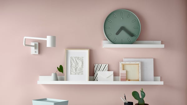 MOSSLANDA picture ledge on a pink wall, these are decoration, pictures and a clock. A lamp hangs on the wall.