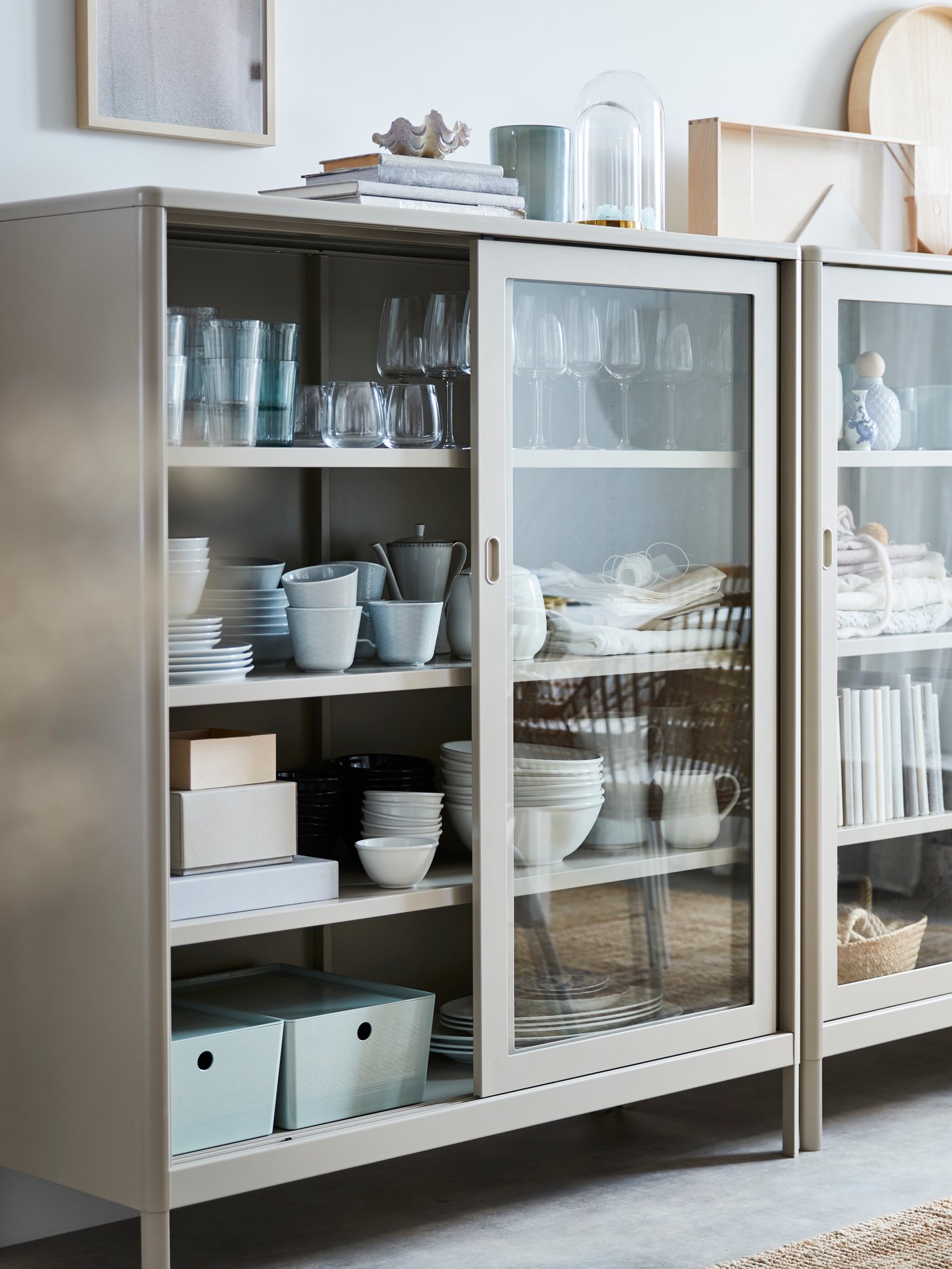 A room with white walls and floorboards that is empty except for an IDANÄS glass-door cabinet filled with bowls.