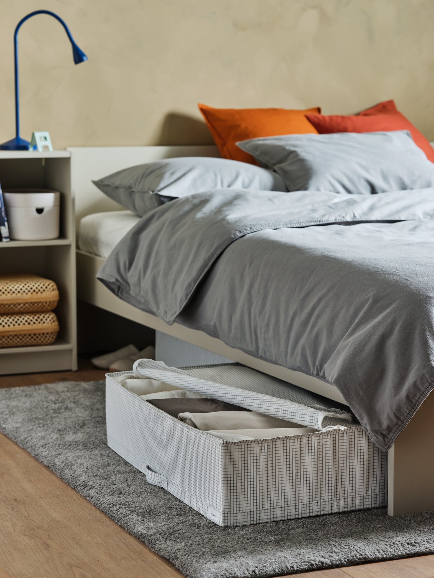 Zona de dormitorio con una caja de almacenaje rectangular en la base de una estructura de cama con cabecero vestida con un juego de funda nórdica.