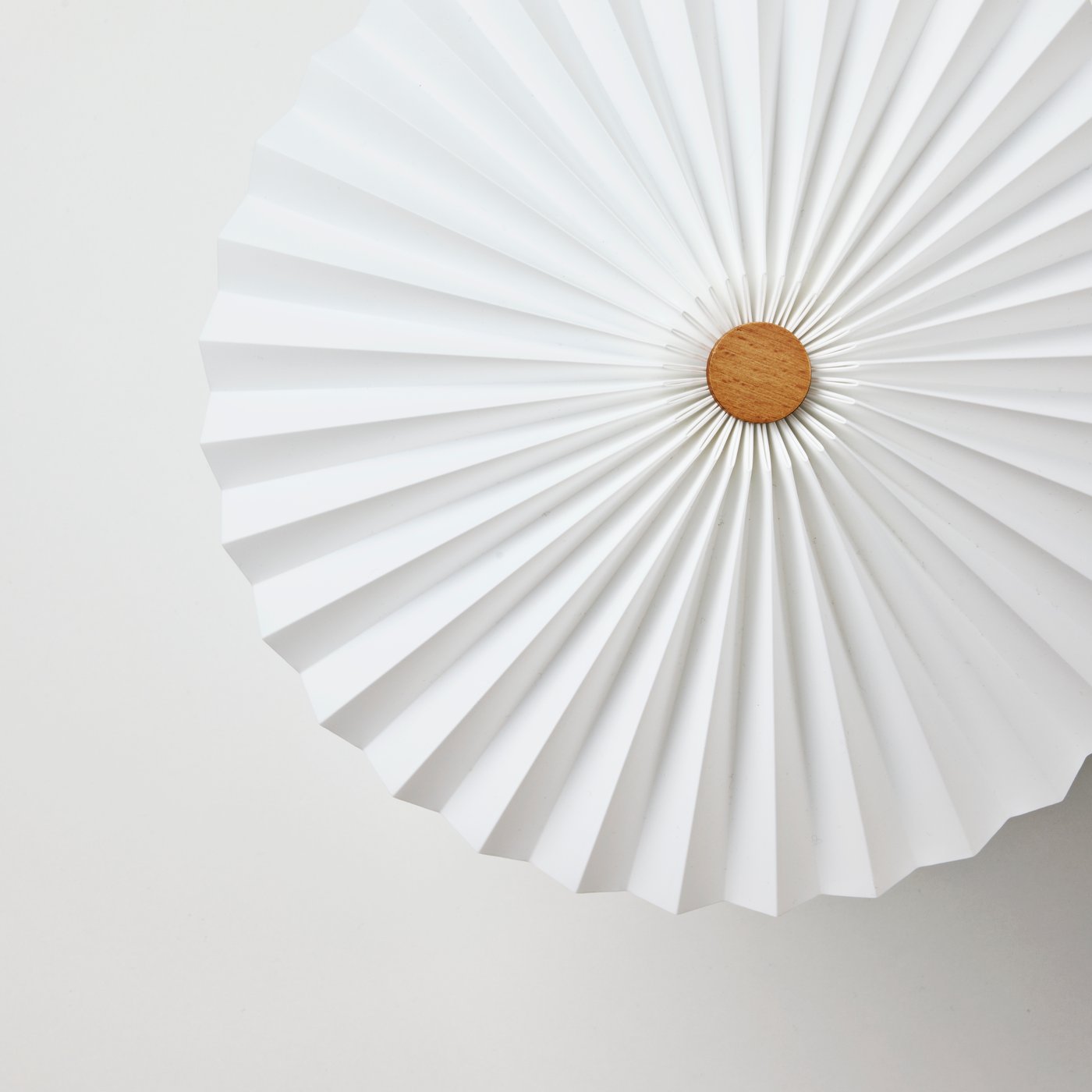 The top of a white KUDDLAVA table lamp, with light playing in the pleats of the circular shade around a central birch knob.