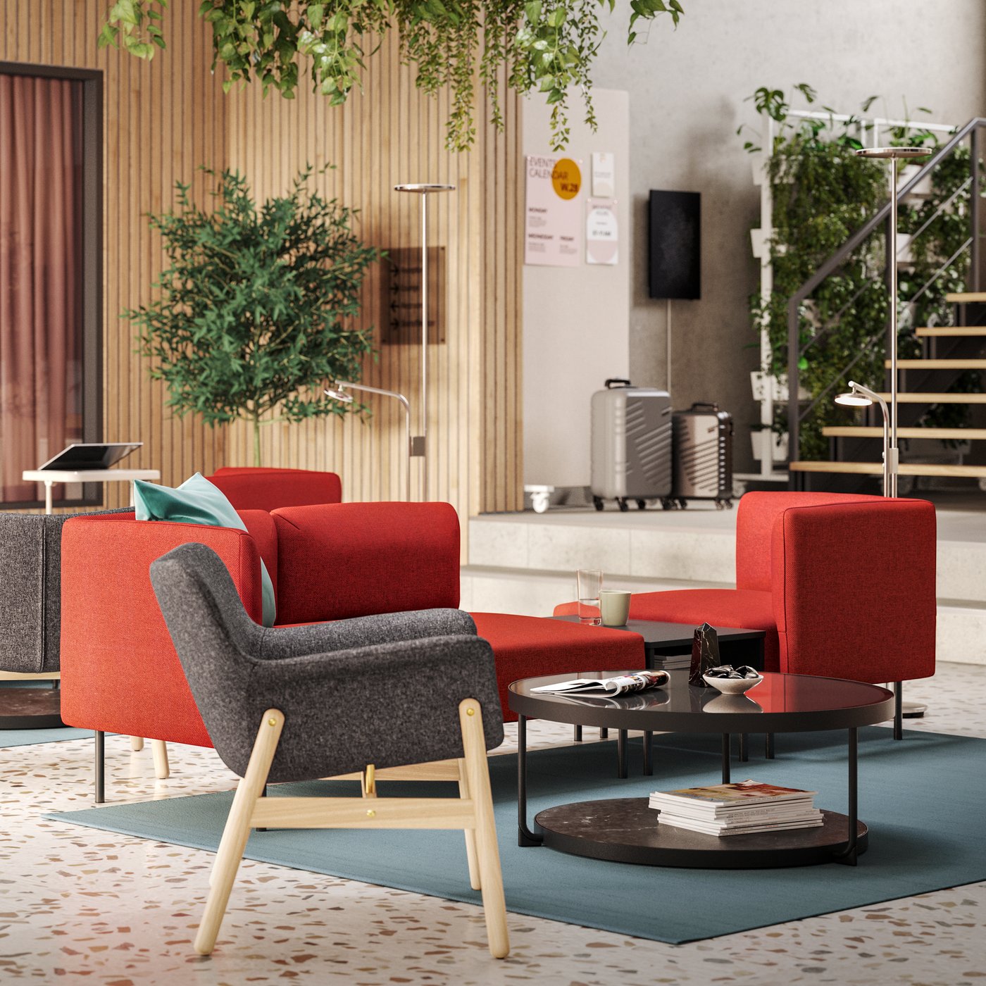 Seating groups with dark grey VEDBO armchairs and red modular sofas are in the middle of a light-filled, modern hotel lounge.