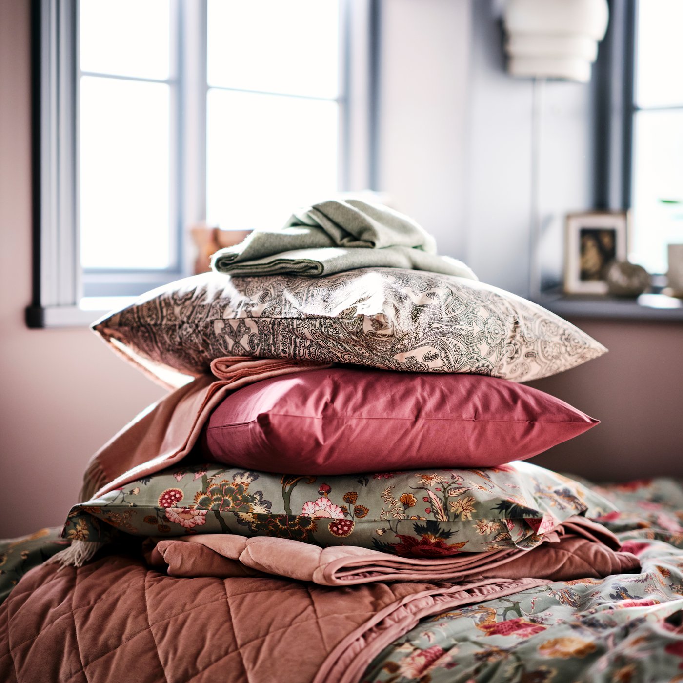A pile of three scatter cushions, one with a JÄTTEVALLMO pillowcase, on the corner of a bed with a NÄSSELKLOCKA duvet cover.