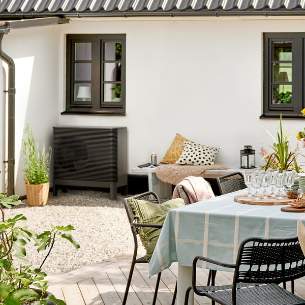 Ein Haus von außen, davor steht ein Tisch mit Stühlen und an der Wand ist eine Luft-Wasser Wärmepumpe zu sehen.