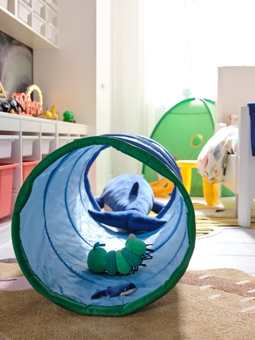 A blue DVÄRGMÅS play tunnel with a green KLAPPA caterpillar toy is placed next to a tray storage unit and a wadrobe.