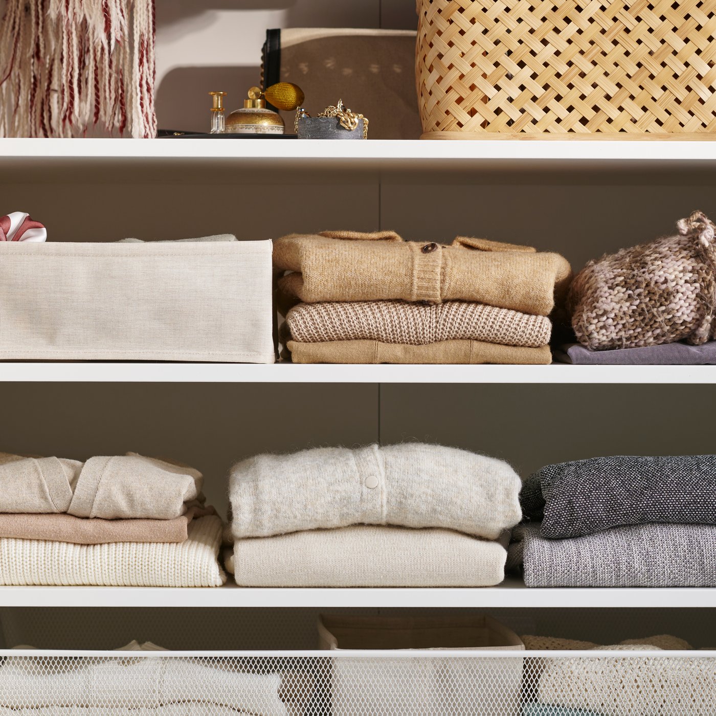 A close up of shelves in a white PAX wardrobe with folded sweaters, VIELÅNGEN box with lid and PURRPINGLA box.