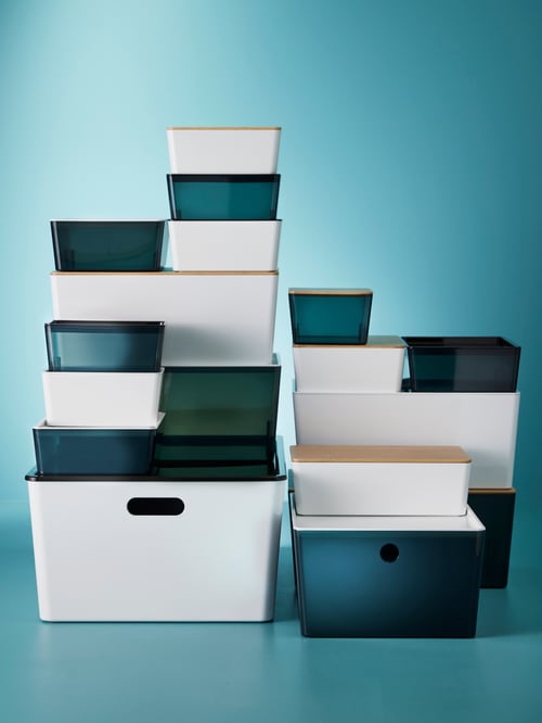Two stacks of rectangular, white and transparent KUGGIS boxes with lids, of various sizes placed against a blue background.