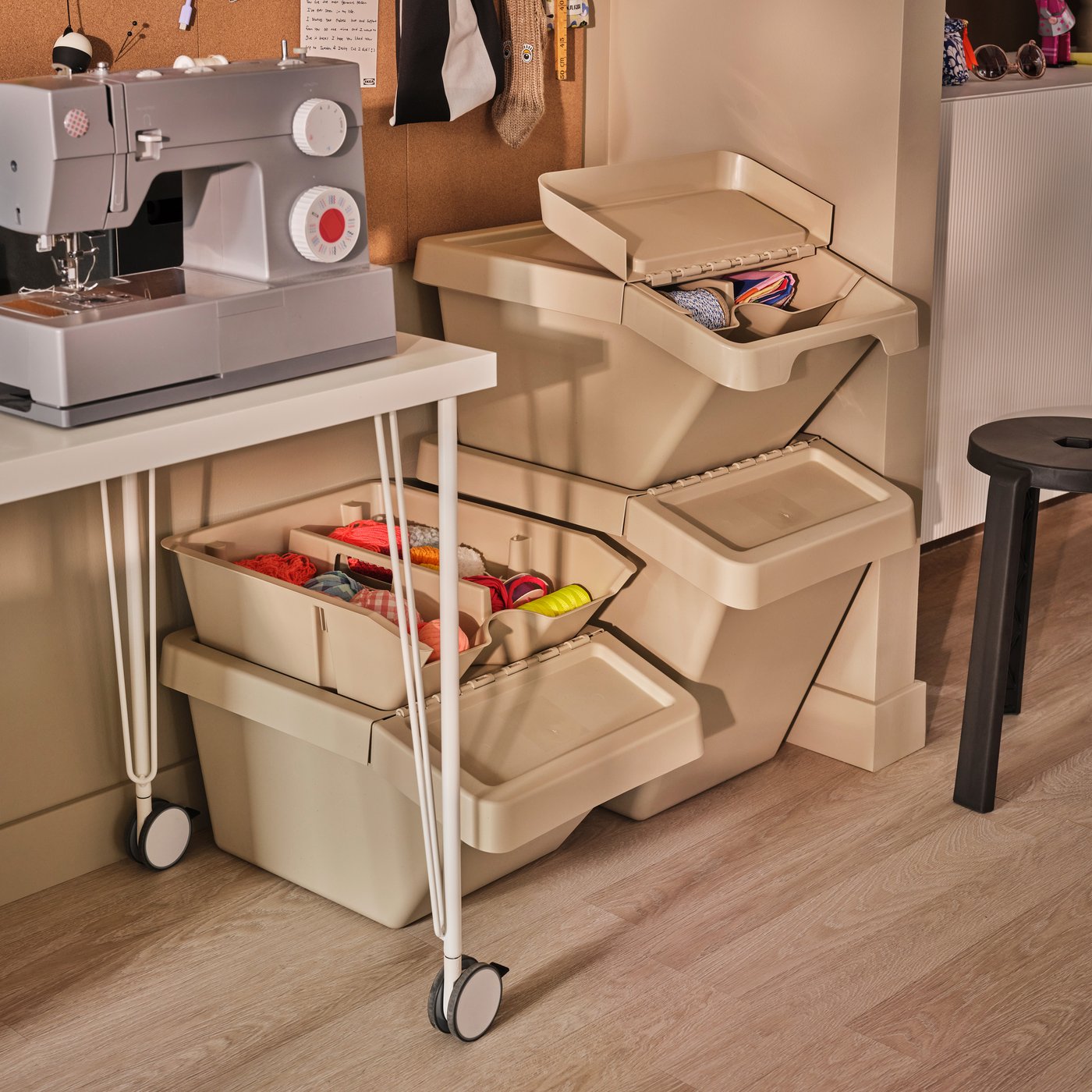 A room with a sewing machine on a table and beige SORTERA sorting bins with lids arranged nearby, filled with supplies.