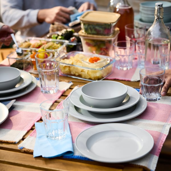A table with people around it has a combination of plates and bowls from the SIMKRABBA series of plastic dinnerware.