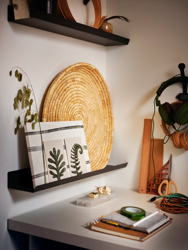 A desk placed into a corner, with decorative objects placed on dark-grey MALMBÄCK display shelves on the wall above.