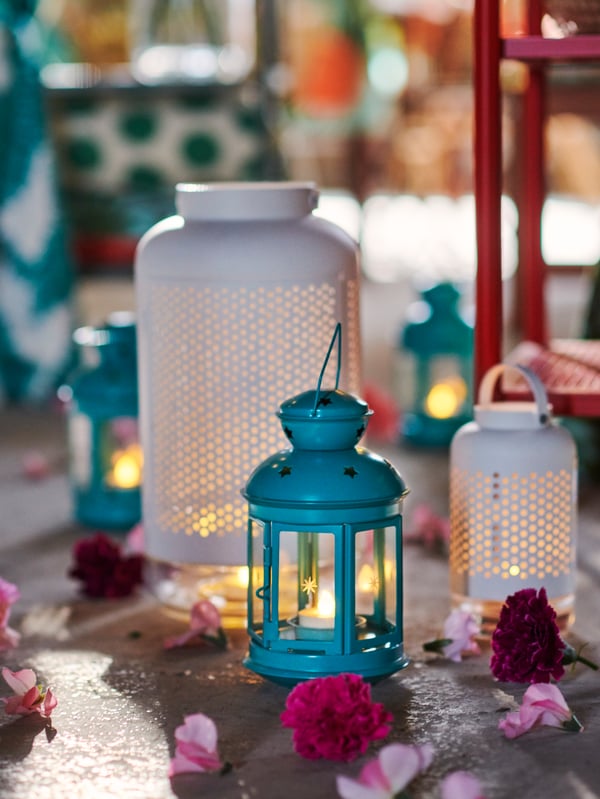 Patch of rough floor with ROTERA and ÄDELHET lanterns placed on it, flowers and petals strewn around them.