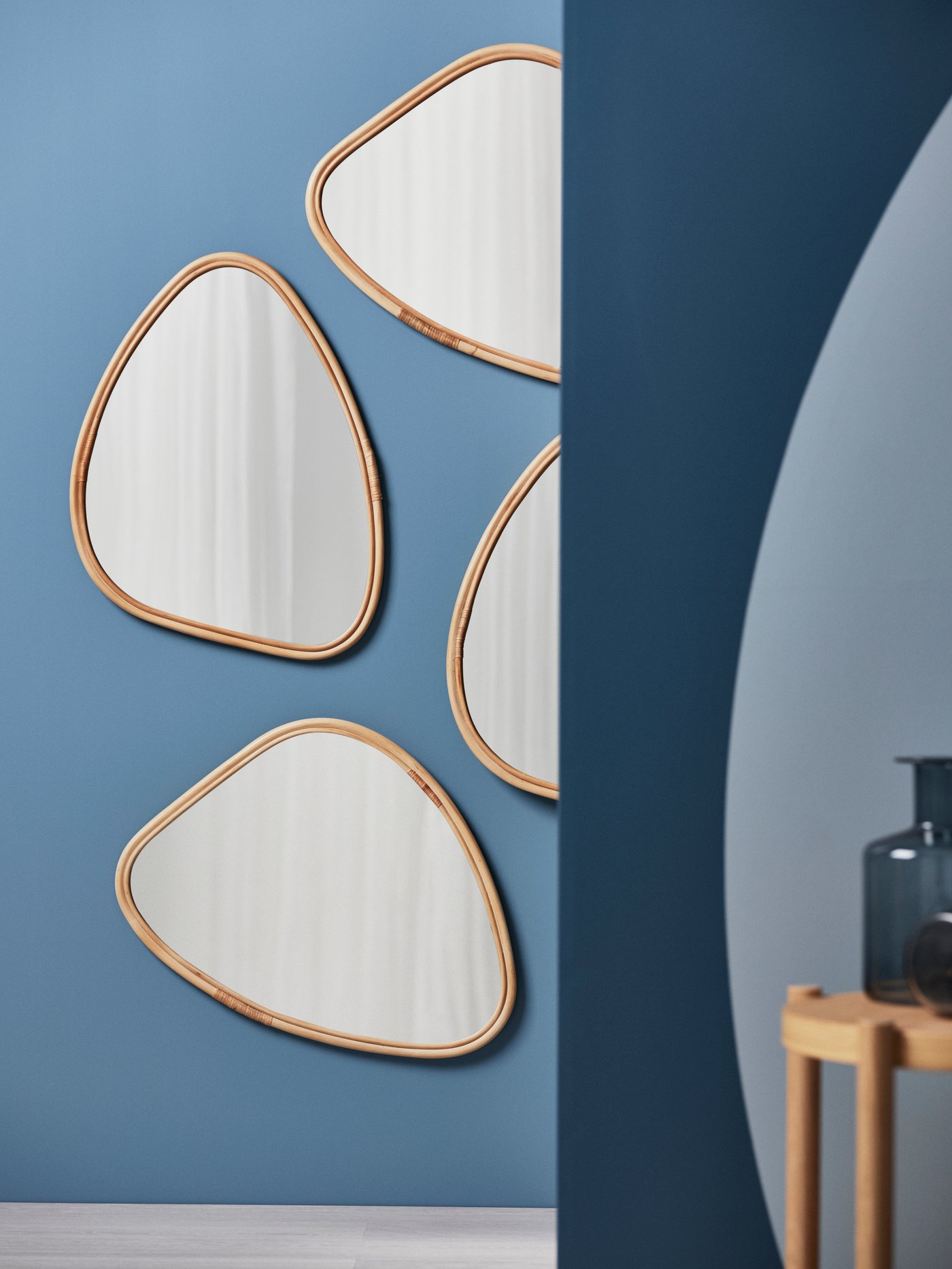 Un tavolino LISTERBY in rovere impiallacciato accanto a una parete azzurra con quattro specchi con cornici in rovere impiallacciato.