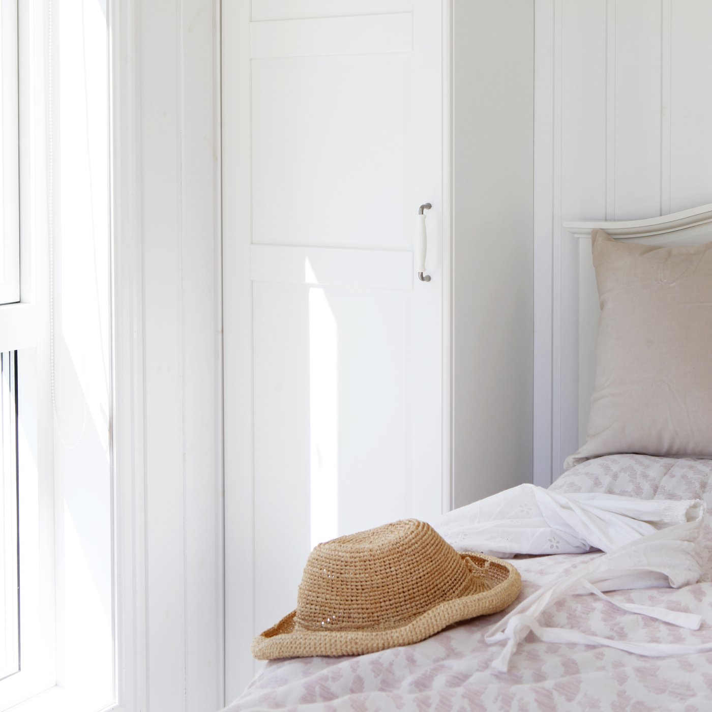 Et soveværelse med hvide træpaneler og en stråhat placeret på blomstret sengetøj på sengen.