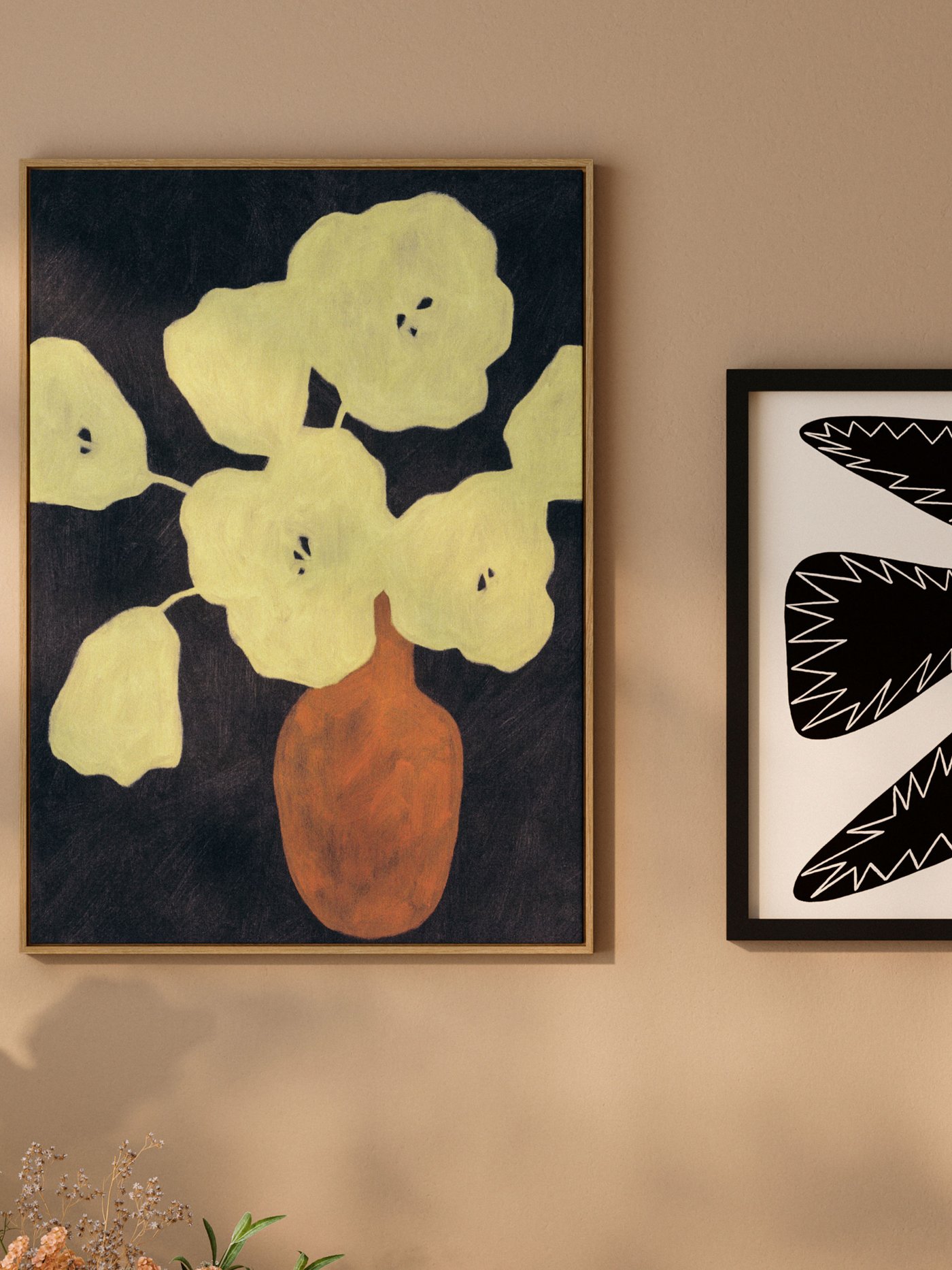 En inramad tavla med gula blommor och en vas hänger på en ljus vägg bredvid en annan grafisk poster.