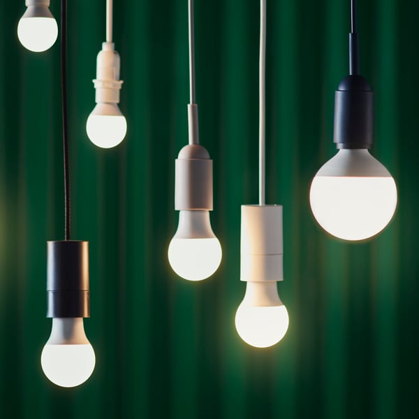 Six different LED bulbs hang from a ceiling with black chords and against a dark green background.