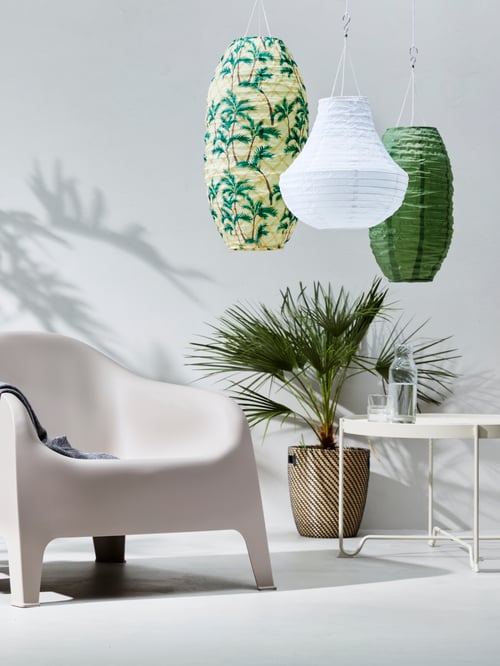 Un espace extérieur avec une table basse, un fauteuil d’extérieur, un cache-pot, une plante, une suspension à DEL à énergie solaire, une bouteille et un verre.