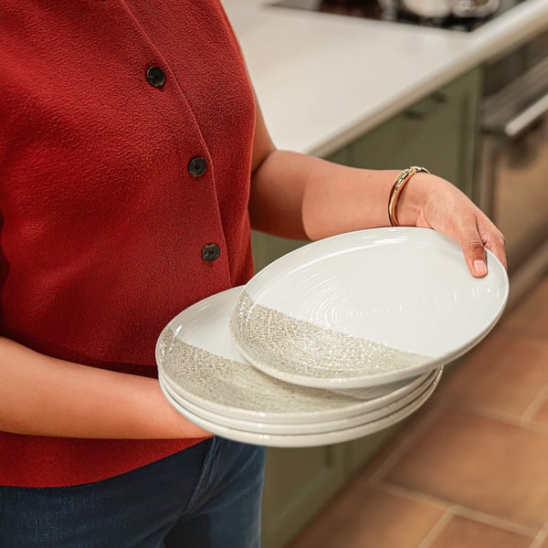 Woman in a red top holding a stack of white plates with textured gray detailing in a modern kitchen setting.