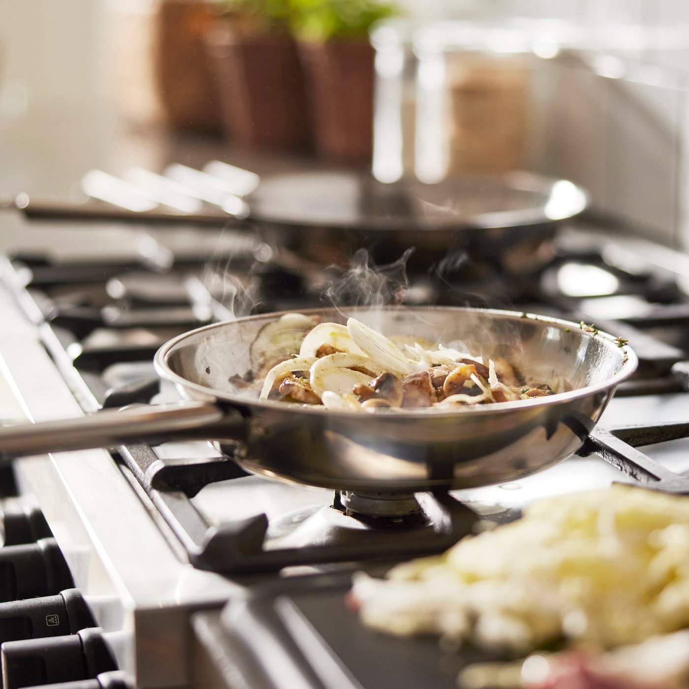 Steaming onions and mushrooms cooking in a stainless-steel pan on a gas stove.
