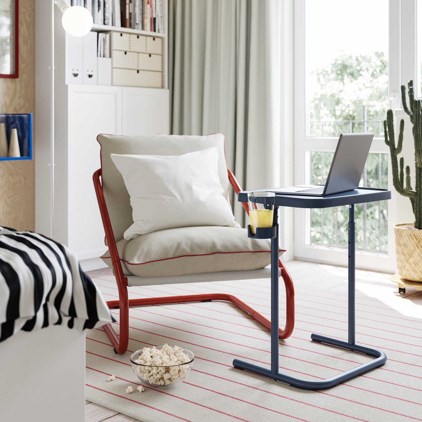 An armchair with a BJÖRKÅSEN laptop stand in blue in front of it, with a cup of juice in the holder.