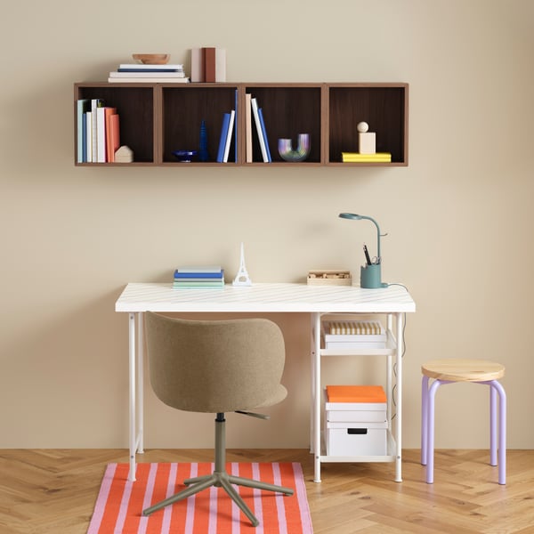 A multicoloured LAGKAPTEN tabletop on white SPÄND legs, paired with a swivel chair and a walnut-effect brown EKET cabinet.