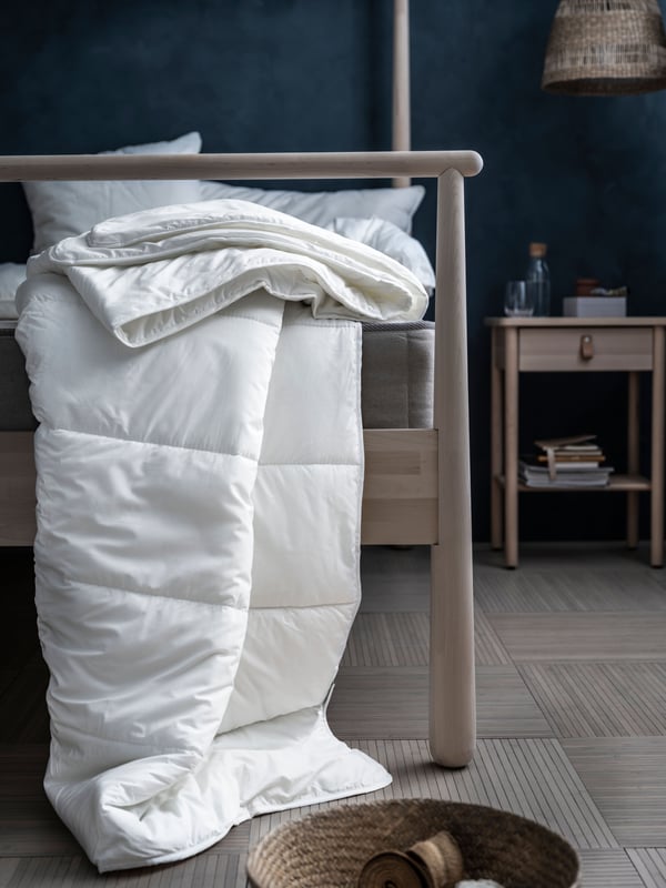 Bedroom with a white duvet draped from the foot end of the GJÖRA bed frame down to the wooden floor. BJÖRKSNÄS bedside table.