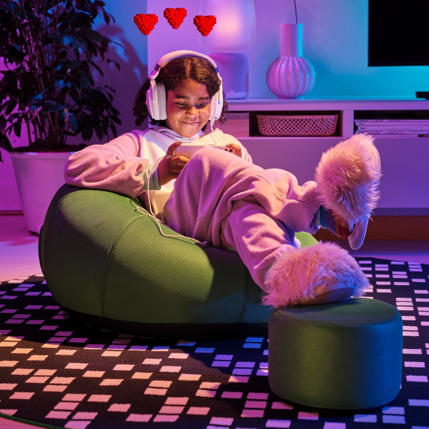 Une jeune fille portant un casque d’écoute est assise sur un fauteuil poire et regarde une manette qu’elle a en main.